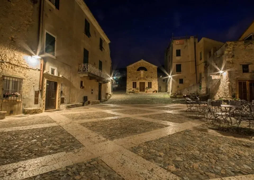 Piazza storica di Borgio Verezzi illuminata di notte con chiesa e case in pietra, entroterra di Finale Ligure.